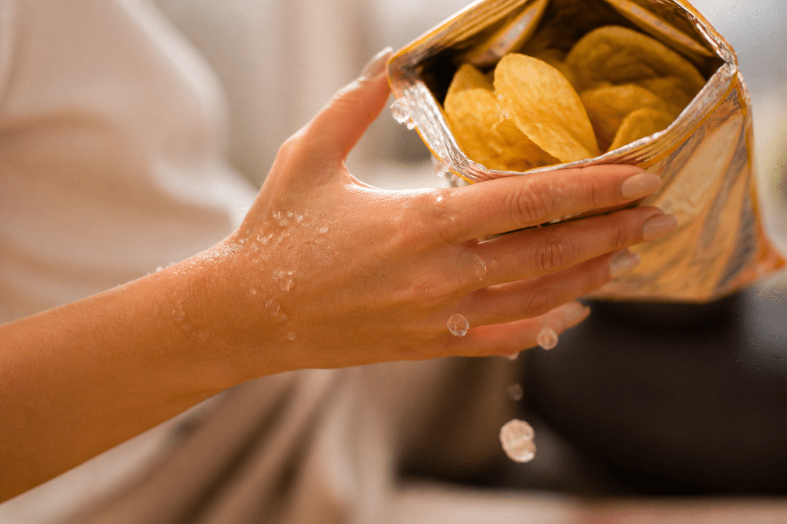 Hand hält Chipstüte, symbolisiert Wassereinlagerungen durch versteckte Salze in verarbeiteten Lebensmitteln.