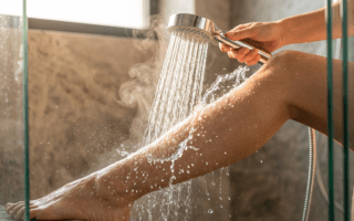 Nahaufnahme eines weiblichen Beins unter wechselnden warmen und kalten Wasserstrahlen in einer Dusche, die die Hautstraffung visualisiert.
