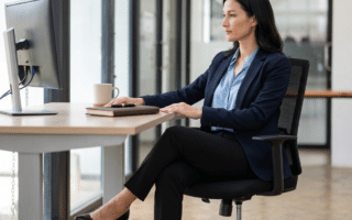 Anti-Cellulite-Training im Büro: 5 unsichtbare Übungen für den Schreibtisch: Frau in elegantem Büro, die unsichtbares Anti-Cellulite-Training im Büro am Schreibtisch ausführt.