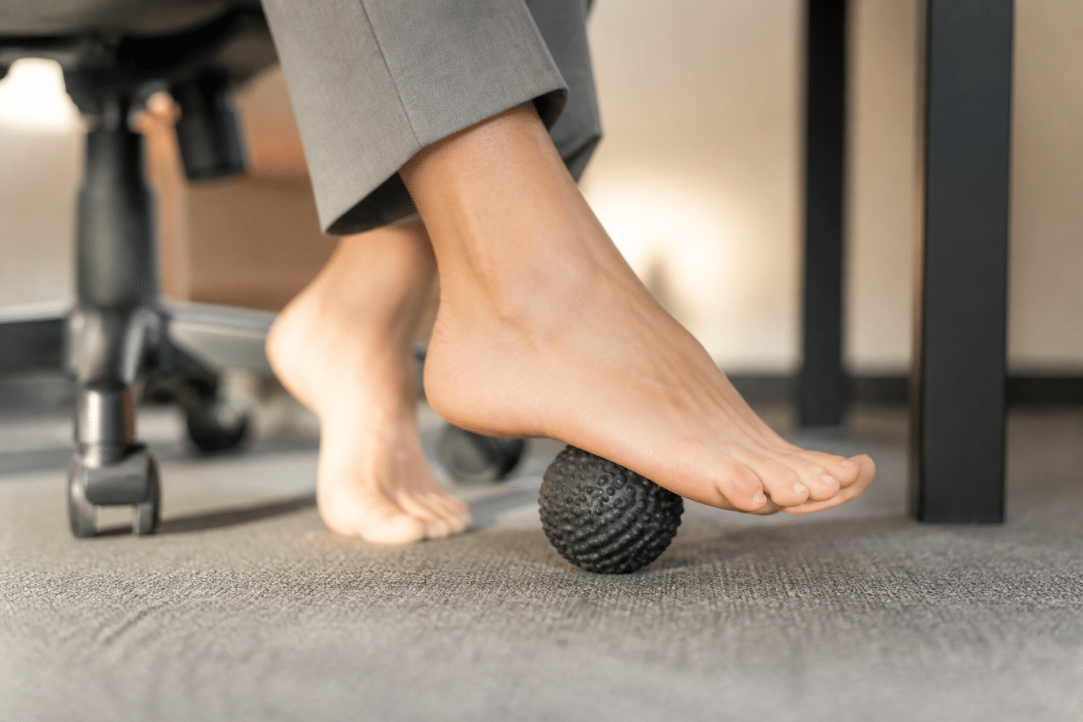 Nahaufnahme der Füße einer Frau, die ihre Fußsohlen auf einem Massageroller stimuliert, um den Lymphfluss anzuregen.