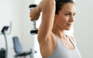 Winkearme ade: Die 5 effektivsten Hantel-Hacks gegen Cellulite an den Oberarmen: Nahaufnahme einer Frau, die eine Hantelübung für den Trizeps ausführt, für straffe Oberarme und gegen Cellulite.
