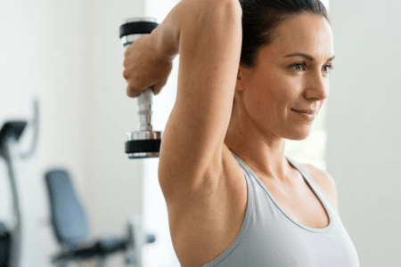 Winkearme ade: Die 5 effektivsten Hantel-Hacks gegen Cellulite an den Oberarmen: Nahaufnahme einer Frau, die eine Hantelübung für den Trizeps ausführt, für straffe Oberarme und gegen Cellulite.